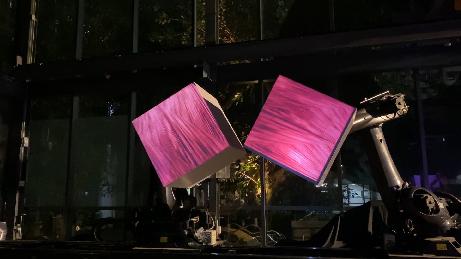 Robotic arm holding two projected cube surfaces in a nighttime performance.